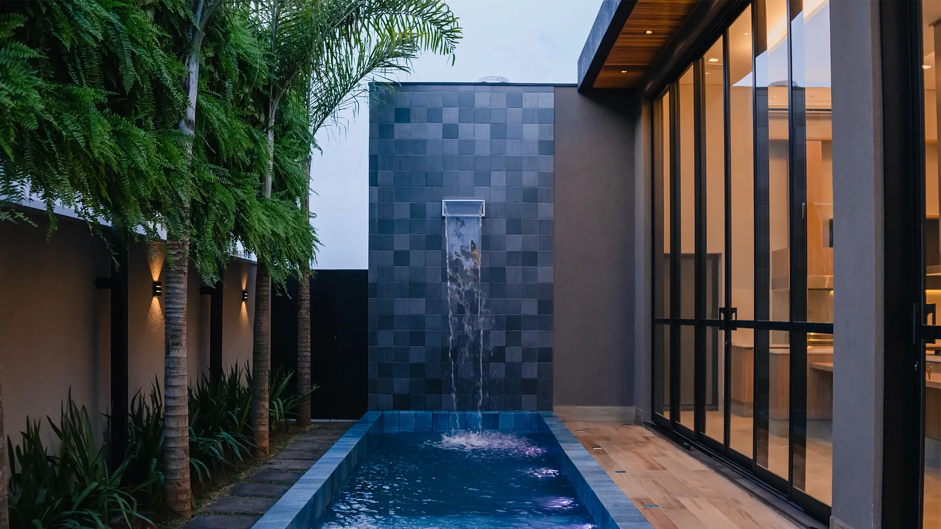 Uma piscina com cascata no quintal de uma casa.